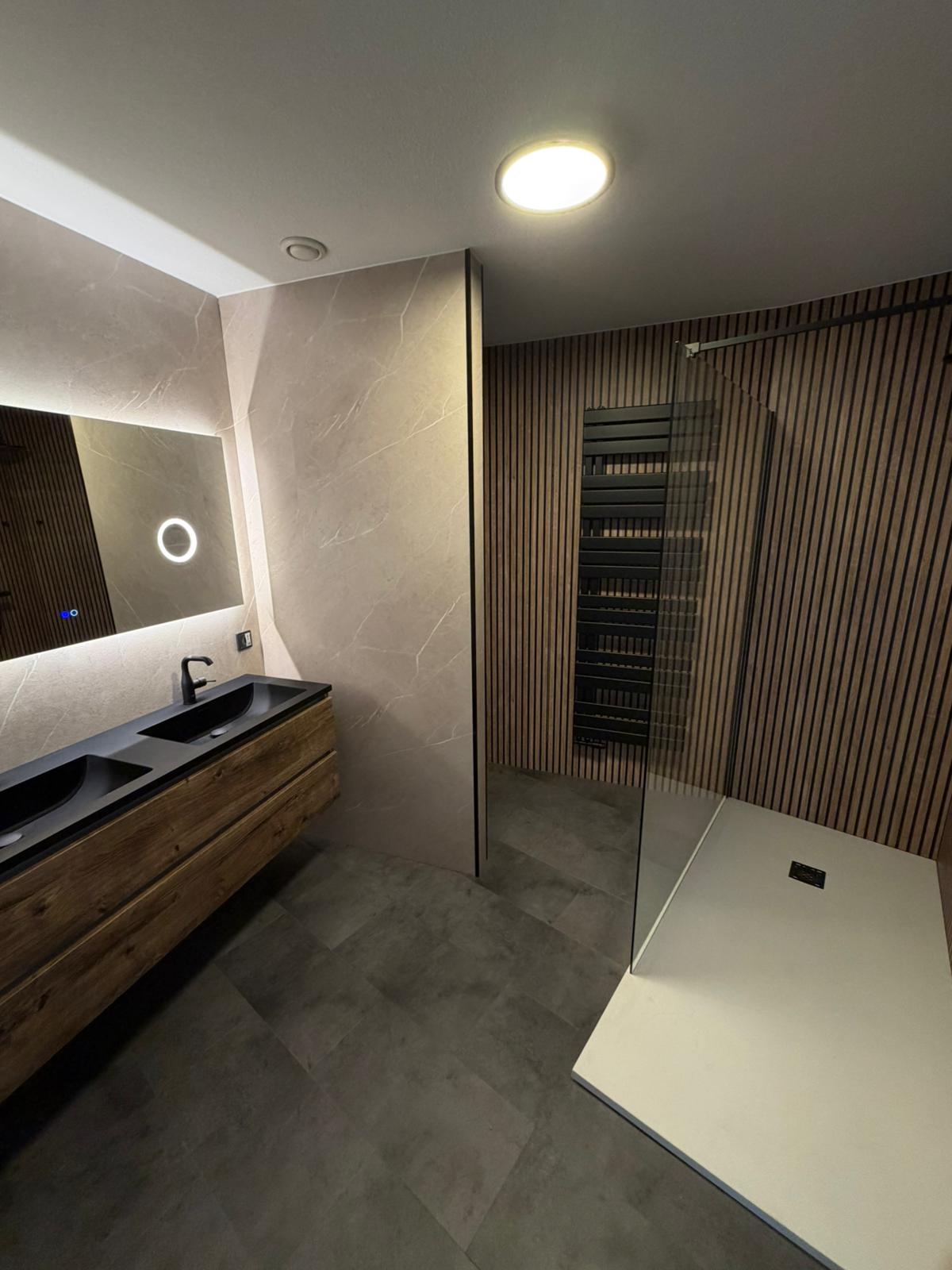 Moderne badkamer met houtlook wandpanelen, marmerlook tegels en een dubbele wastafel met LED-spiegel.