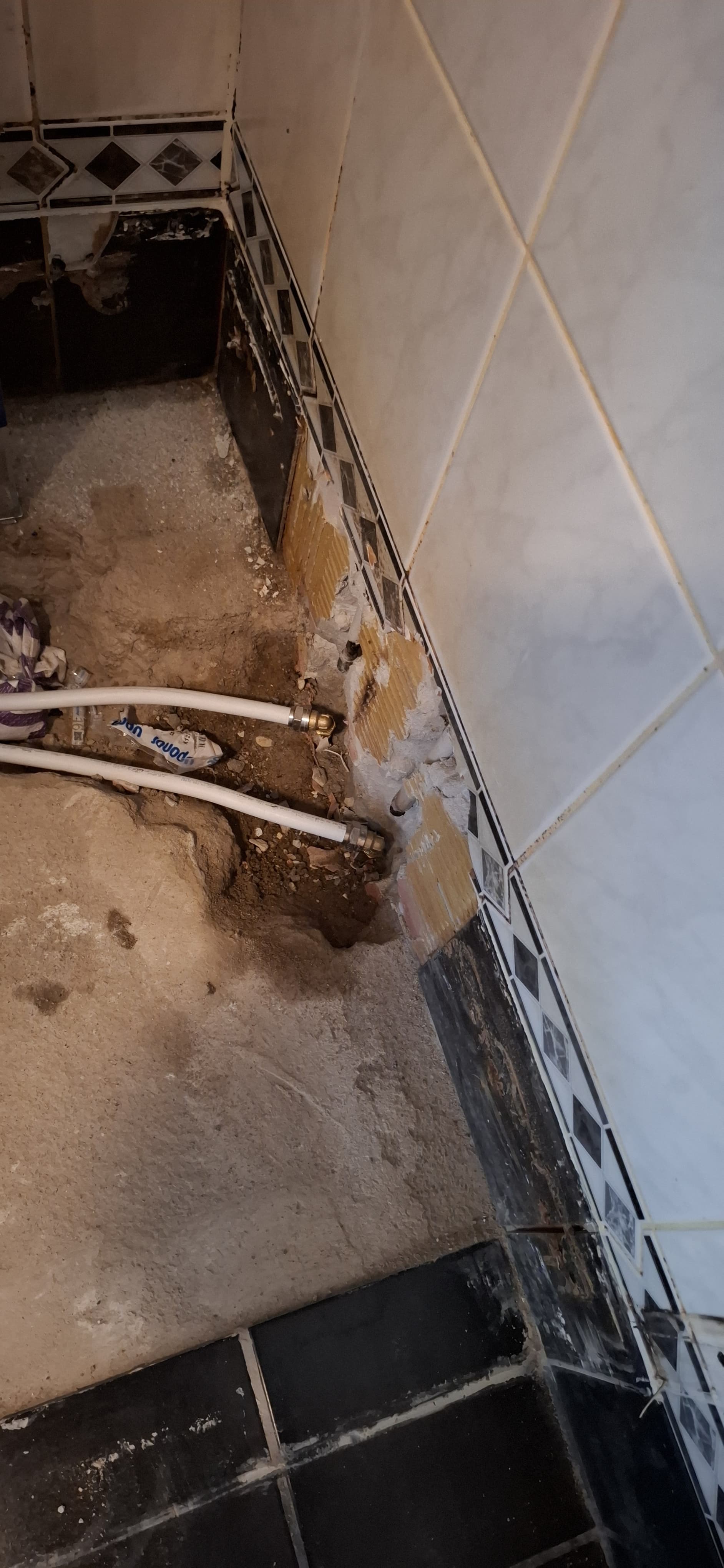 Badkamerrenovatie: blootgelegde leidingen in een badkamer met zwart-wit geblokte tegels.